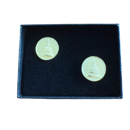 Gold-colored cufflinks with a detailed design on a black box, placed on a wooden surface.